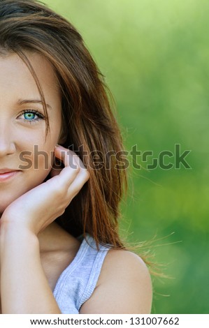 Portrait of beautiful smiling young woman close up, against background of summer green park.