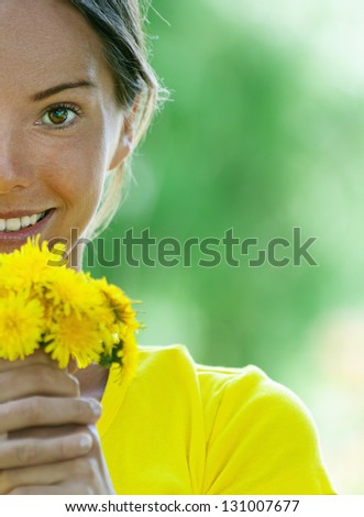 Portrait half of dark-haired smiling beautiful young woman in yellow blouse with a bouquet of dandelions, against green of summer park.