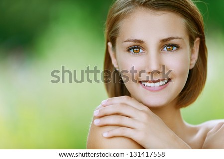 Portrait of smiling beautiful young woman close up, against background of summer green park.