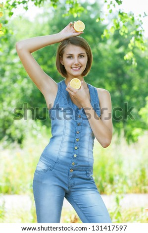Portrait of smiling beautiful young woman with lemon, against background of summer green park.