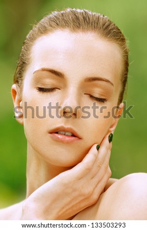 Portrait of beautiful young woman with her eyes closed, against green of summer park.