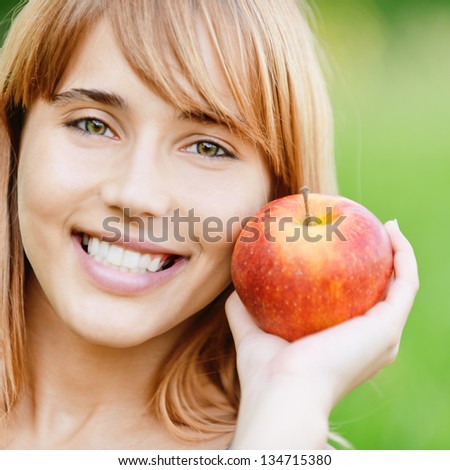 Beautiful young cheerful woman with red big apple, against green summer garden.