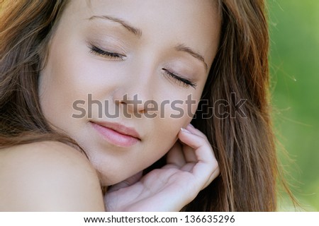 Portrait of beautiful young woman close up with eyes closed, against background of summer green park.