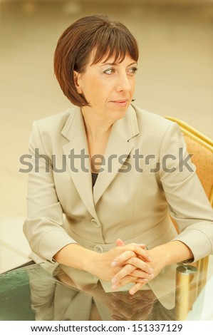 Beautiful businesswoman in bright suit sitting at glass table.
