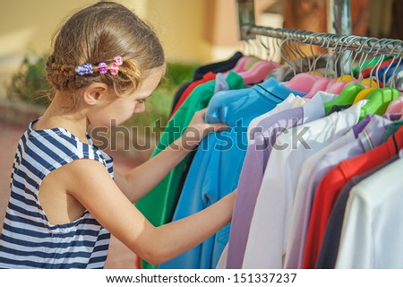 Little beautiful girl choose right clothes at store.
