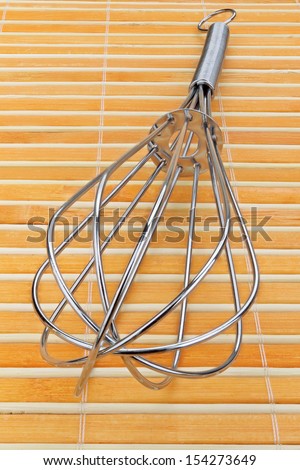 Metal wire whisk in orange bamboo napkin.