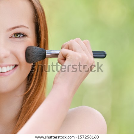 Smiling beautiful young woman with bare shoulders on face powder, against green of summer park.