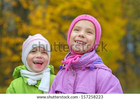 Two young sisters laughing and hugging against of autumn city park.