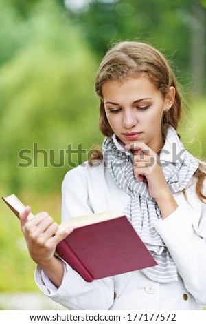 Young happy beautiful woman reading red book, against background of autumn park.