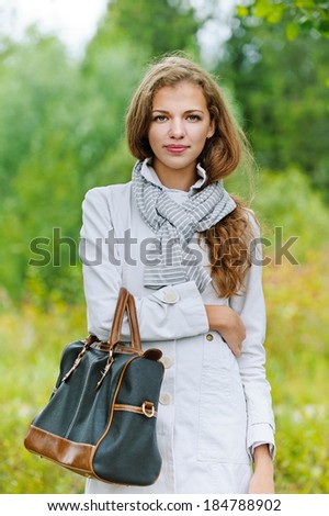 Portrait of nice young woman with handbag, against background of autumn park.