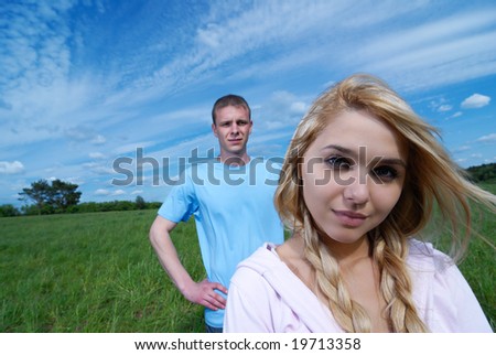 The young beautiful woman and on a distant background the young man on a green field