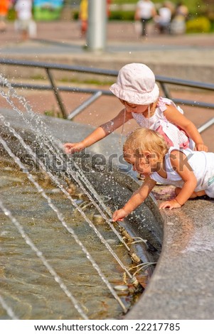 Two little girls have got on protection of fountain and play about with water streams.