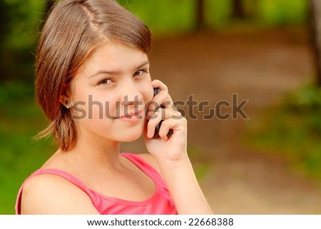 The young beautiful girl talks on a cellular telephone in city park.