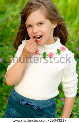 Little girl eats chocolate stick against summer nature.