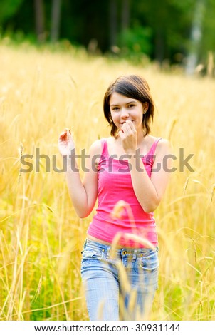 Beautiful girl goes across field among kept up wheat.