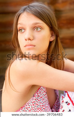 Beautiful girl looks back back, against log house.