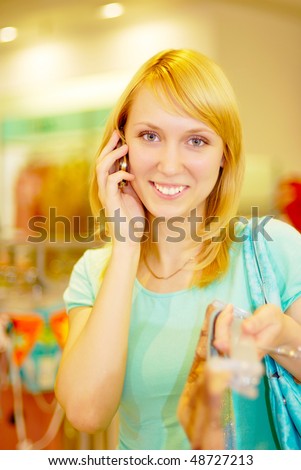 The young beautiful woman laughs and talks by a mobile phone in a supermarket in lady\'s wear section