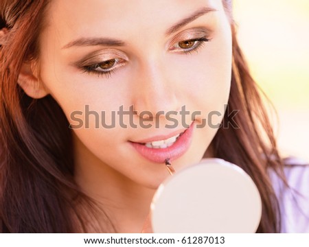 Young woman looks in mirror also paints lips.