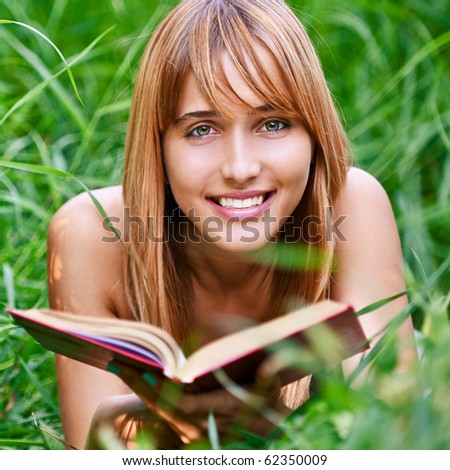 Beautiful young woman reads book, on green summer background.
