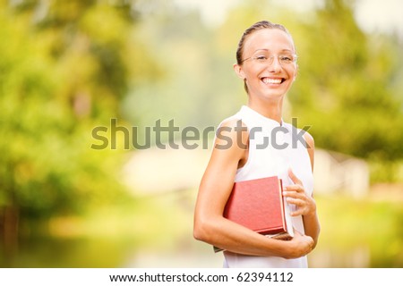 Portrait of beautiful laughing girl-student with book against summer green park.