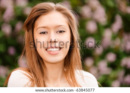 Young beautiful woman with long hair smiles against blossoming bush in city spring park.