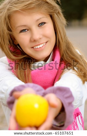 Beautiful young woman stretches big yellow apple.