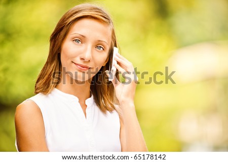 Portrait of beautiful girl which speaks by mobile phone against green summer garden.