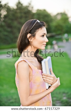Profile girl-student holds textbooks, against summer garden.