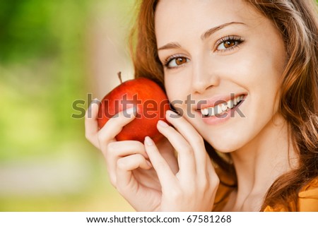 Portrait of girl with red apple against green grass.