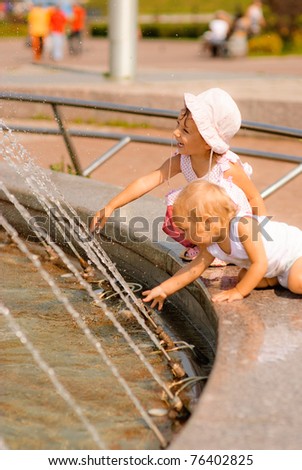 Two little girls have got on protection of fountain and play about with water streams.