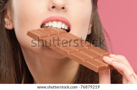 Mouth of beautiful young woman bites off from chocolate brick, on red background.