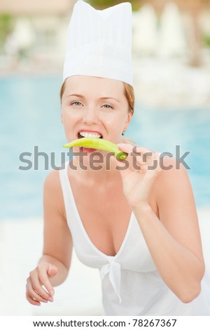 Young beautiful woman-cook tastes food about summer pool on resort.