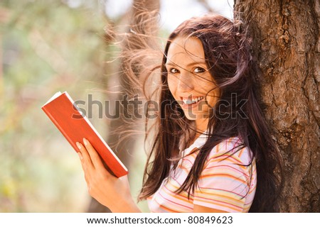Lovely young woman reads book in green summer garden.