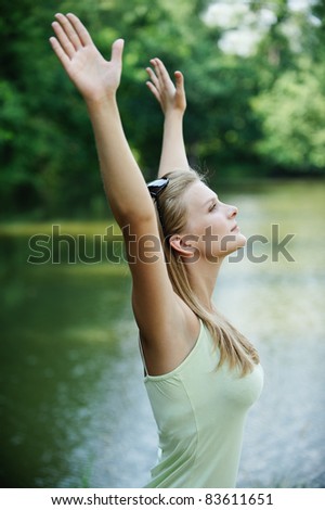 Portrait of young pretty woman holding hands up against lake at summer green park.
