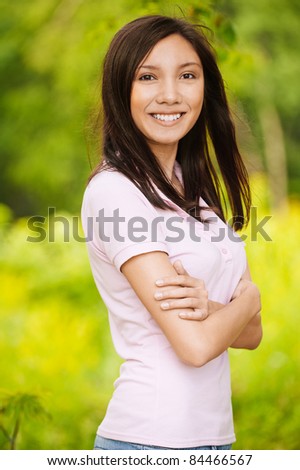 Portrait of young beautiful smiling brunette wearing beige blouse and standing in summer green park.
