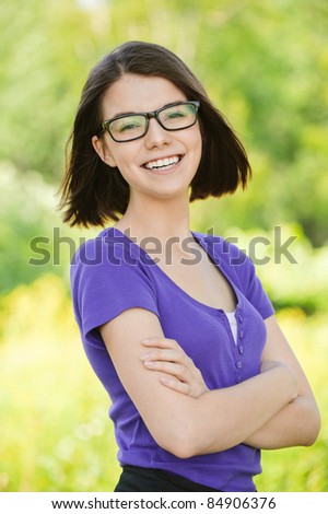 Portrait of young cheerful laughing woman wearing purple blouse and eyeglasses standing at summer green park.