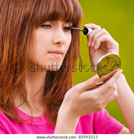 Portrait of young pleasant woman making herself up and looking to mirror.