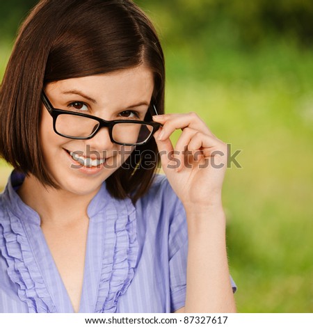 Portrait of young smilling woman wearing violet blouse ang eyeglasses standing at summer green park.
