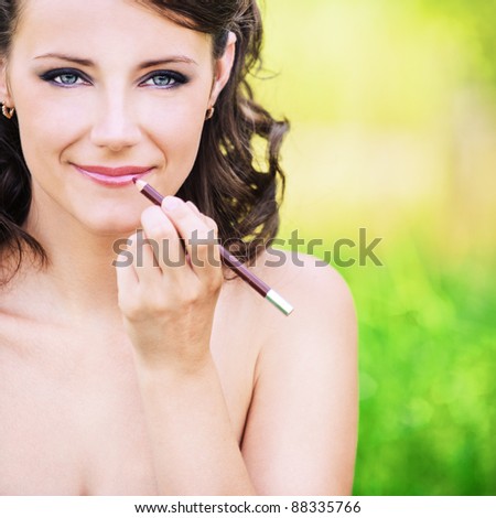 Portrait of charming dark-haired woman making herself up at summer green park.