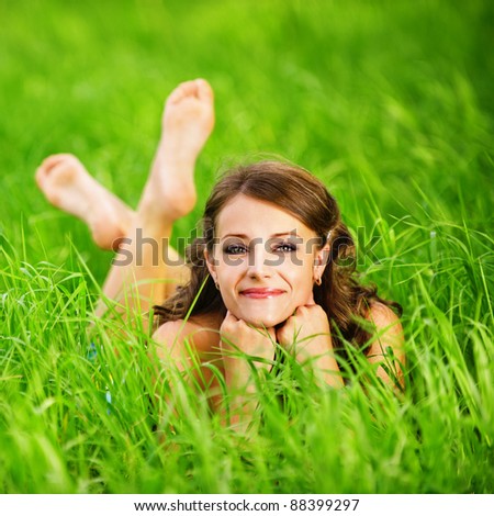 Portrait of young beautiful brunette woman lying on grass and propping up her face at summer green park.