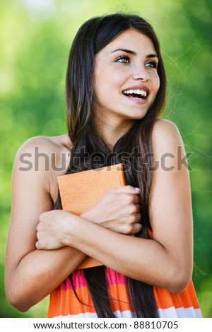 dark hair beautiful young happy student smile chest hugged book background green park