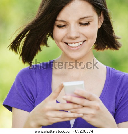 Portrait of young beautiful smiling woman wearing violet blouse with mobile phone at summer green park.