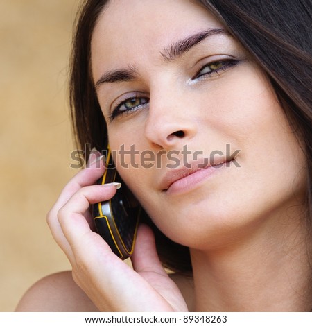 Close-up portrait of young attractive brunette woman speaking on mobile phone against yellow background.
