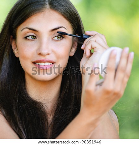 portrait beautiful young woman bare shoulders looks mirror paints eyelashes background summer green park