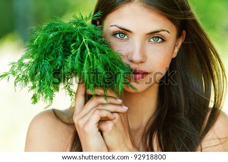 portrait of beautiful young dark-haired sexy girl seductively baring her shoulders with bundle of herbs (dill) in hands