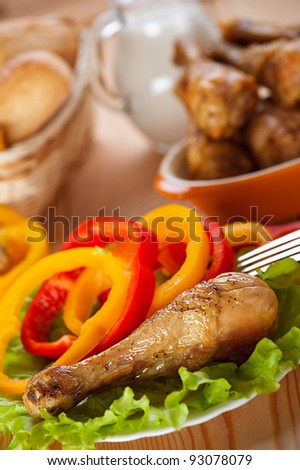 dish of fried chicken drumsticks delicious on lettuce leaves with sliced ??circles of Bulgarian pepper in background transparent glass jug with milk and wicker vase with bread