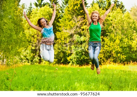 Two young beautiful girls jumps up at summer green park