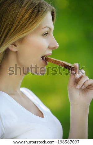portrait of young beautiful woman eating bread in summer green park
