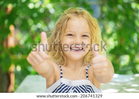 Little cheerful girl lifts thumb upwards, on green background.