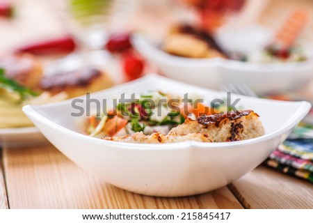 abundance of food on kitchen wooden table on napkin and fork with bowl of salad (radishes, tomatoes, parsley, eggs), meat katlety (pork, beef, lamb)